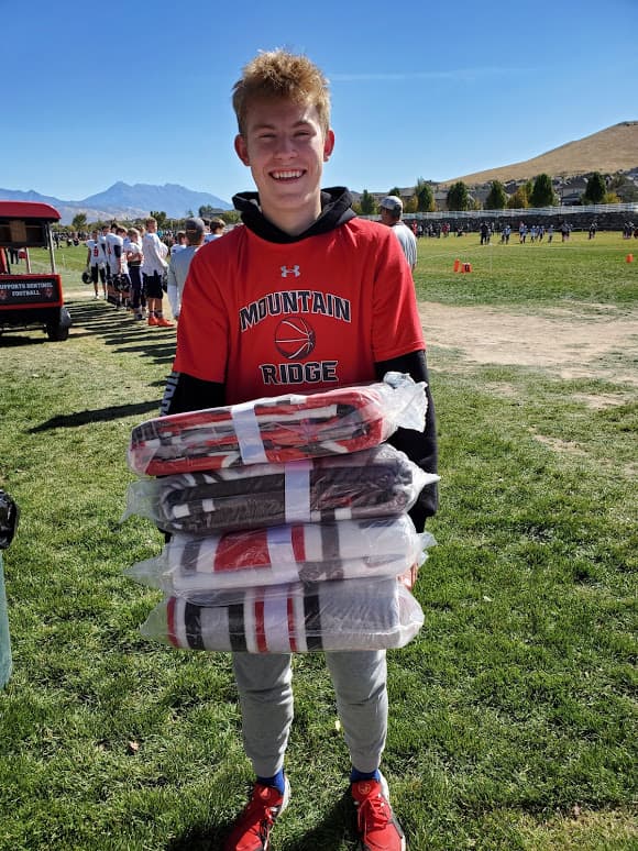 Mountain Ridge HS student in a basketball t-shirt holding a stack of four packaged custom blankets at a school event