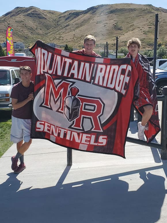 Three Mountain Ridge HS students holding up the custom Mountain Ridge Sentinels banner blanket in front of the Utah mountains