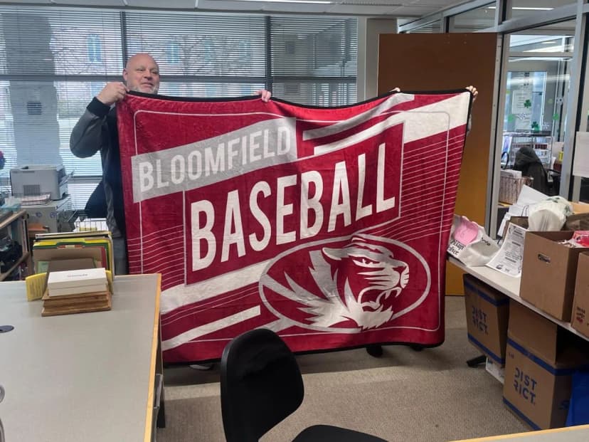 Athletic director holding up a finished Bloomfield Baseball blanket in the school office